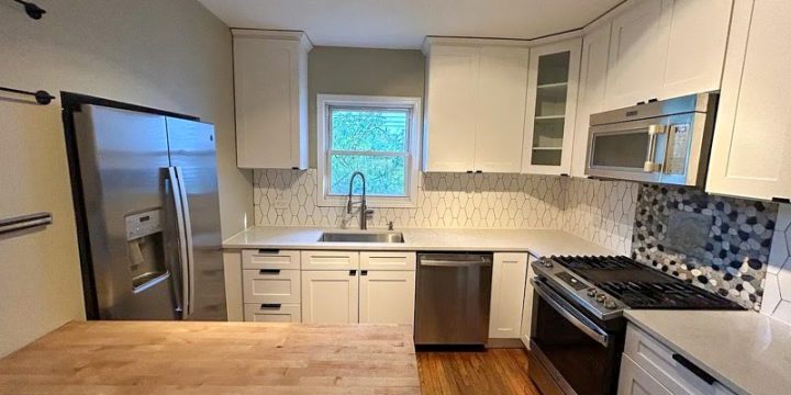 Clean, modern kitchen with white shaker cabinets, white countertops, and a decorative mosaic tile backsplash behind the stainless steel range. Includes GE oven, Maytag microwave, and hardwood flooring — perfect for functional, stylish cooking.